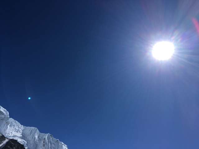 Bright sun in a clear blue sky with mountain peaks.