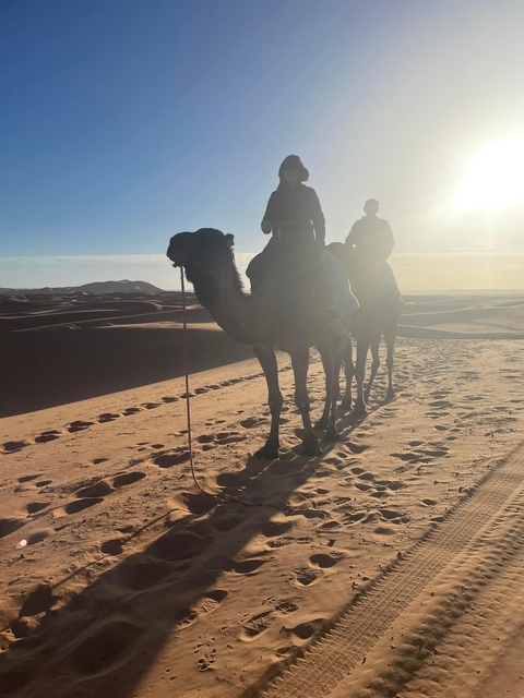 People riding camels on sand dunes at sunset.