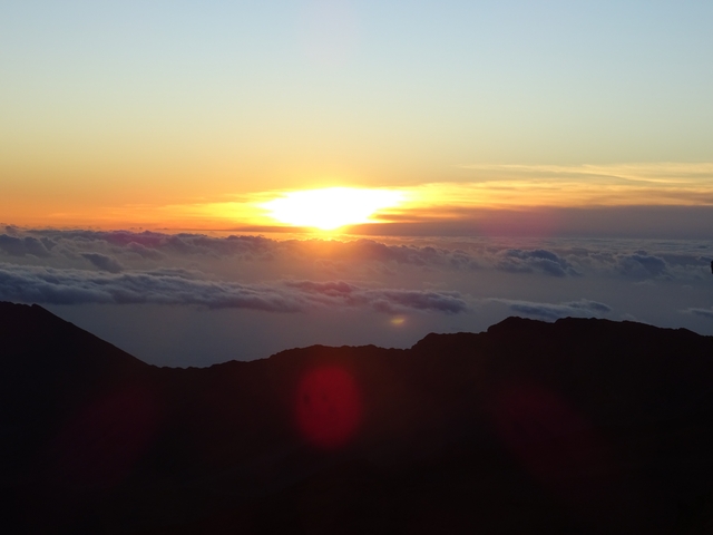 Sunrise view above the clouds with a silhouette of a mountain.