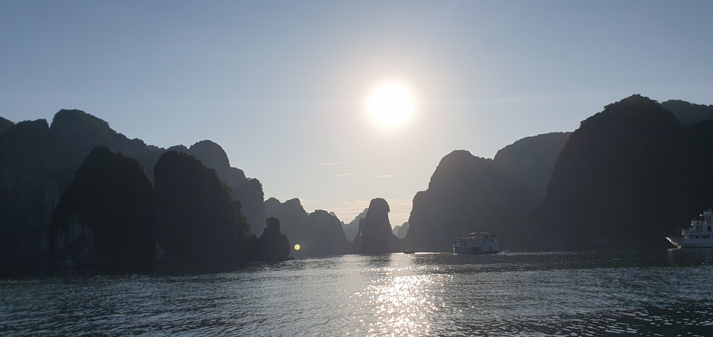 Halong Bay with sunlight reflecting off the water amidst limestone karsts.