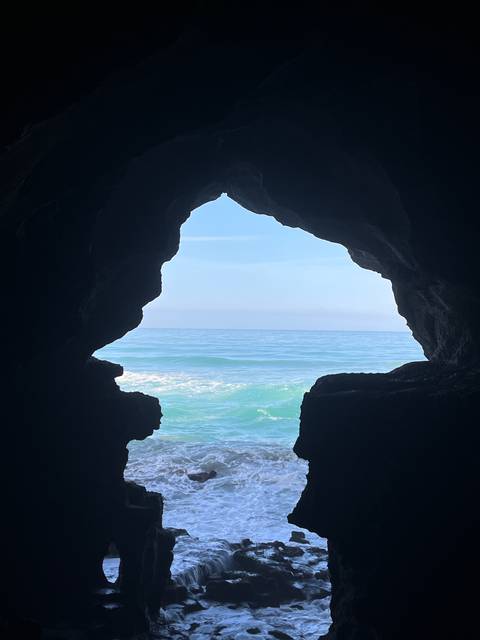 View through a cave opening to the ocean with waves crashing against the rocks.