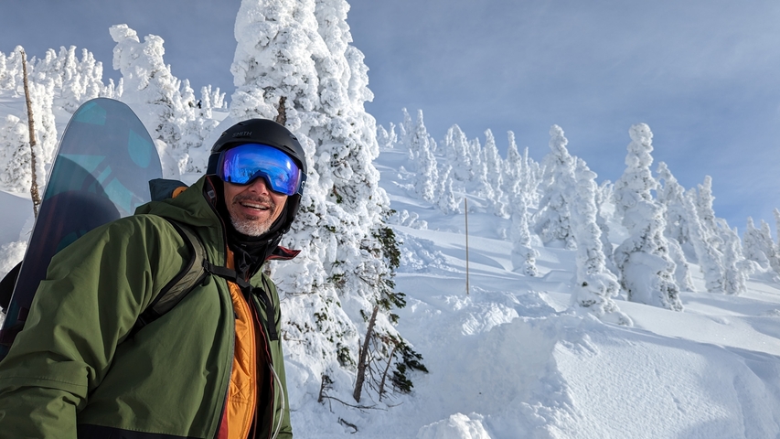 A snowboarder in snowy mountain terrain with frosted trees.