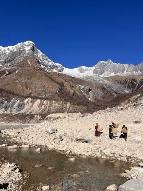 People with carrying baskets in a mountainous Himalayan landscape.