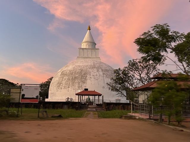 Large white dome-shaped stupa under a pink sky.