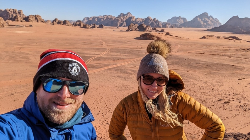 Couple standing in a vast desert landscape with mountains.