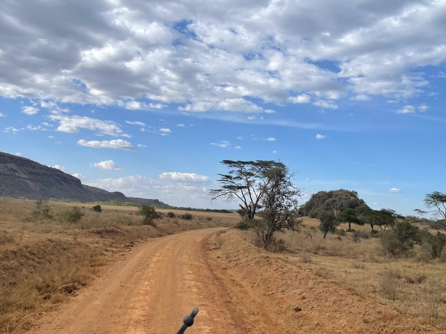 Dirt road in a sparse, open landscape with a distant hill.