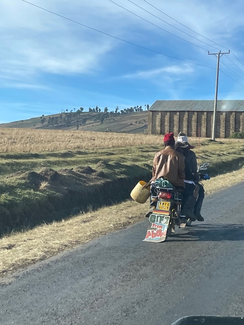 Three people riding a motorbike on a rural road.