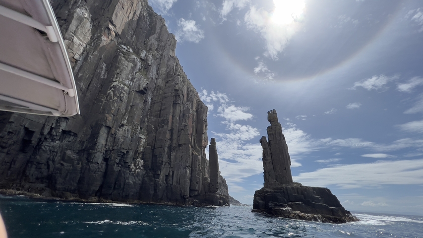 Dramatic rock formations by the sea under a bright sky.