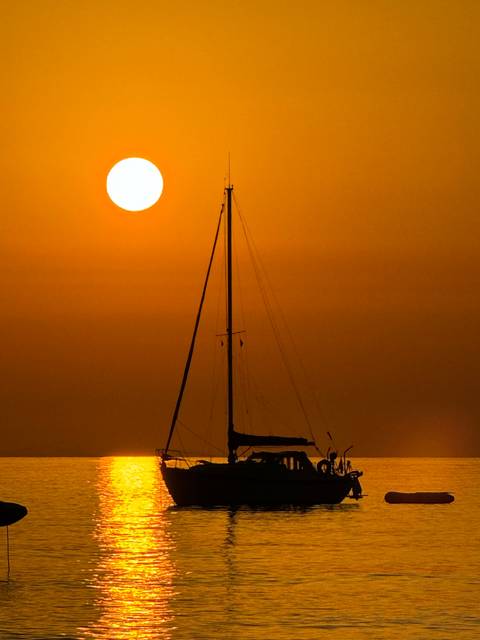 Silhouette of a sailboat during a vivid orange sunset.