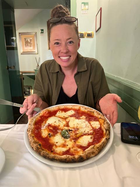 Woman holding a pizza in a restaurant setting.