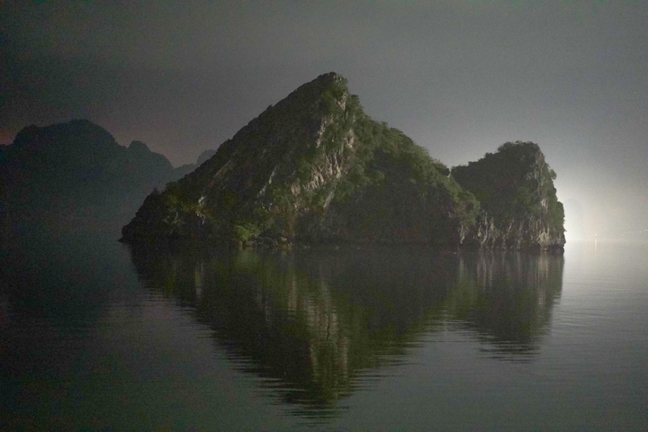 Steep rocky island with reflection in water at night.