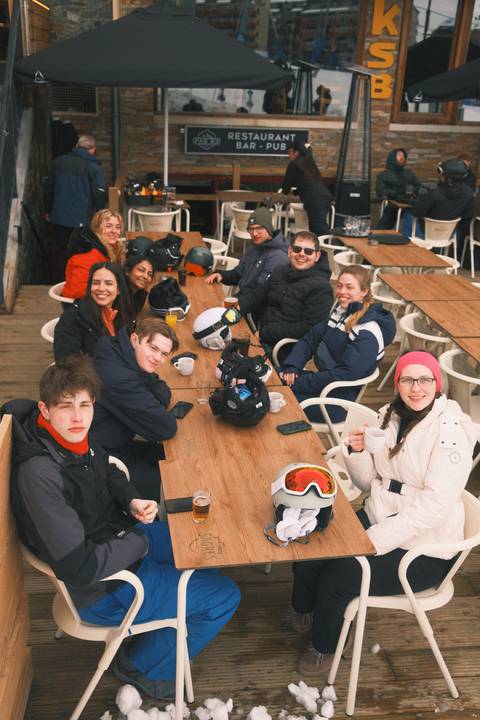 Group of people sitting at an outdoor café table in winter clothing.