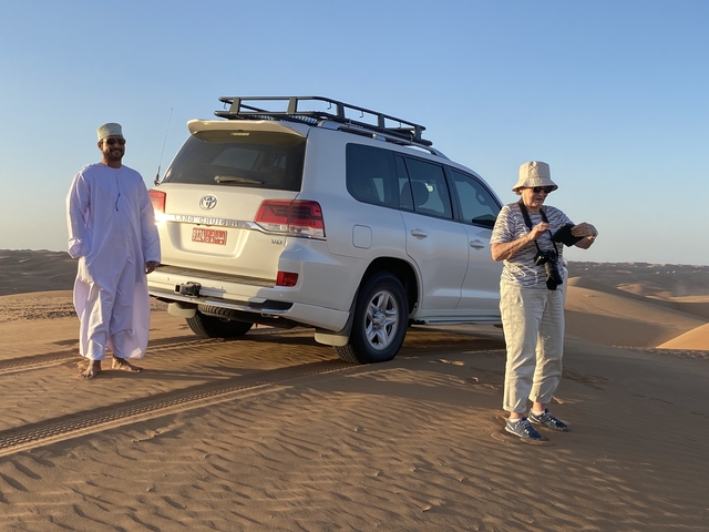 People with a car parked on sandy dunes.