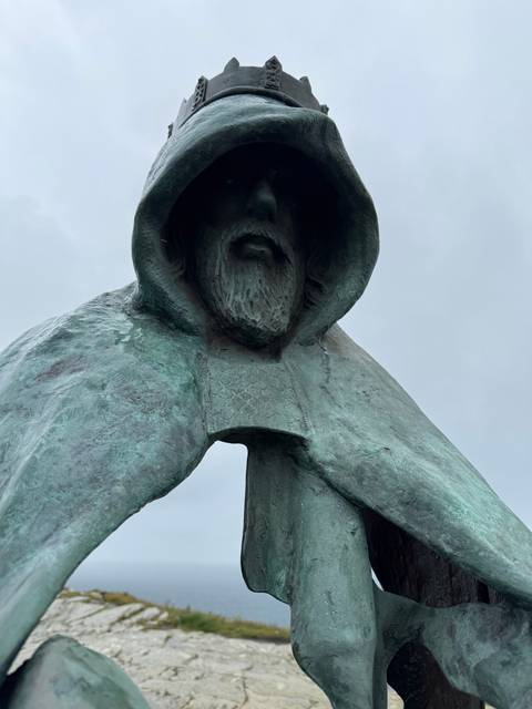Statue of a robed figure holding a sword with a coastal backdrop.
