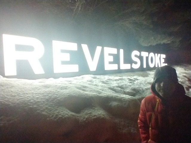 Person in front of a backlit Revelstoke sign in the snow.