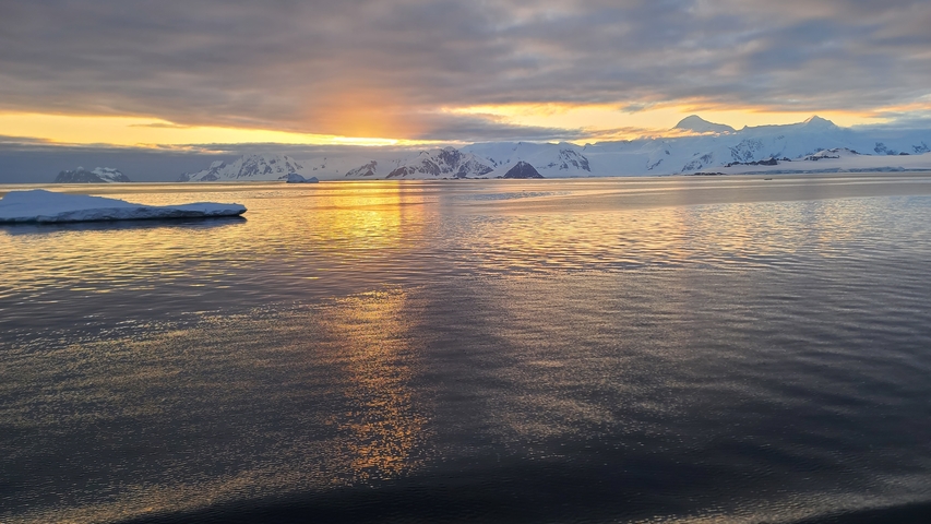 Ocean view with icebergs and a vibrant sunset sky reflecting on the water.
