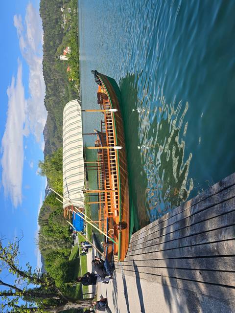 A wooden boat docked beside a clear blue lake with mountains in the background.