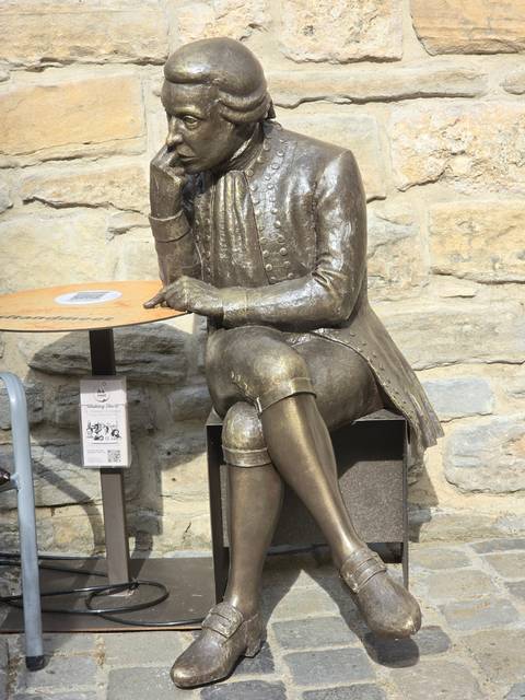 Bronze statue of a person sitting thoughtfully on a chair.