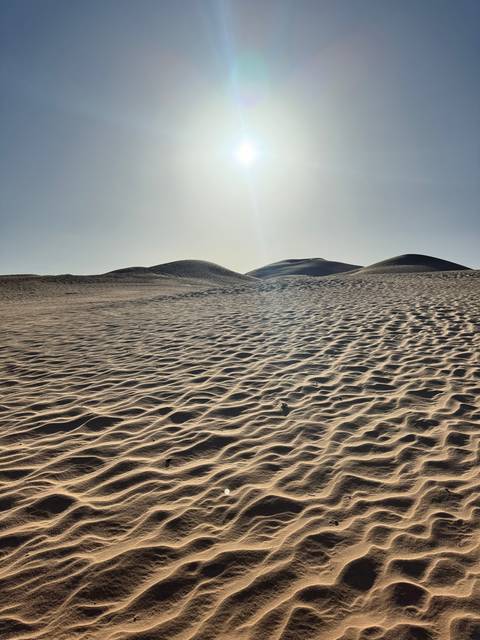 Sandy dunes with the sun overhead.