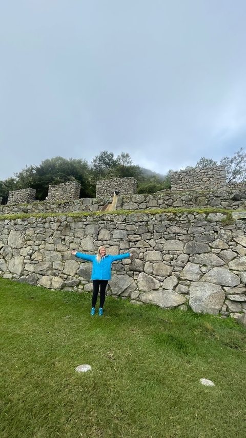Person posing in front of stone terraces with a llama.