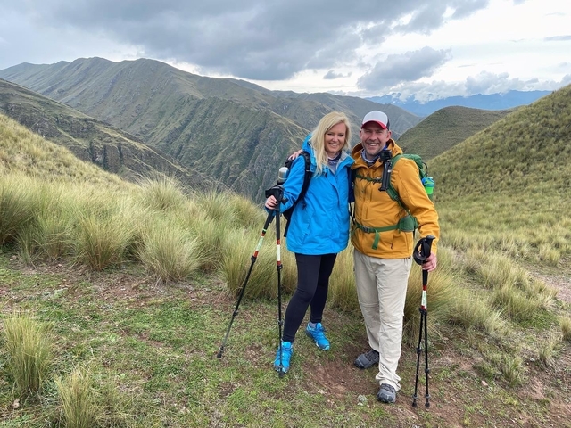 Couple posing on a scenic mountain trail with trekking poles.