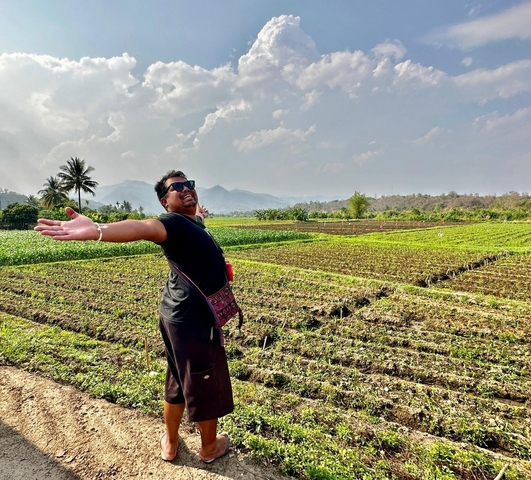 Person standing in a field, spreading their arms wide.