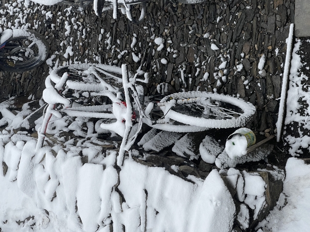 Bicycle covered in snow leaning against a wall.