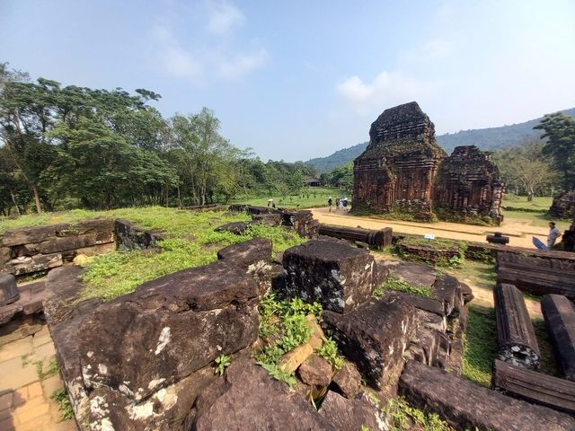 Ancient ruins with visitors exploring the site amidst lush greenery.