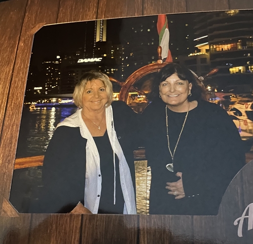 Two people standing on a boat at night with cityscape in the background.