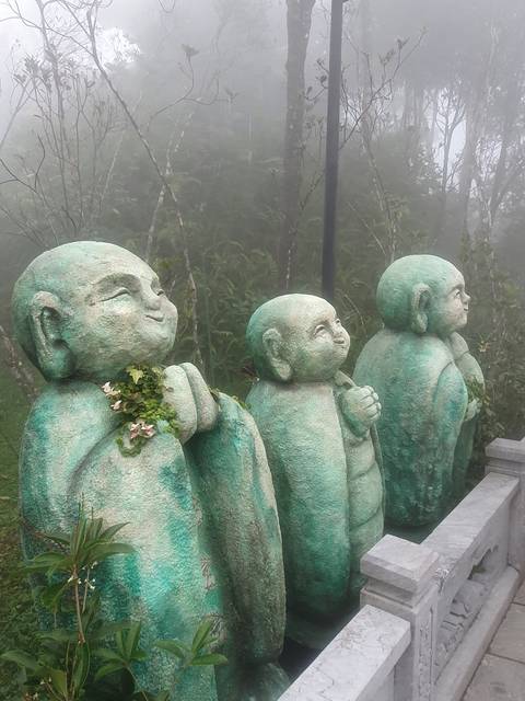 Several green statues of children in a misty environment.