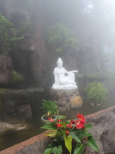 A white statue surrounded by fog and flowers.