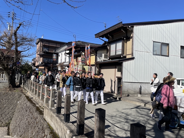 People parading down a street with traditional houses.