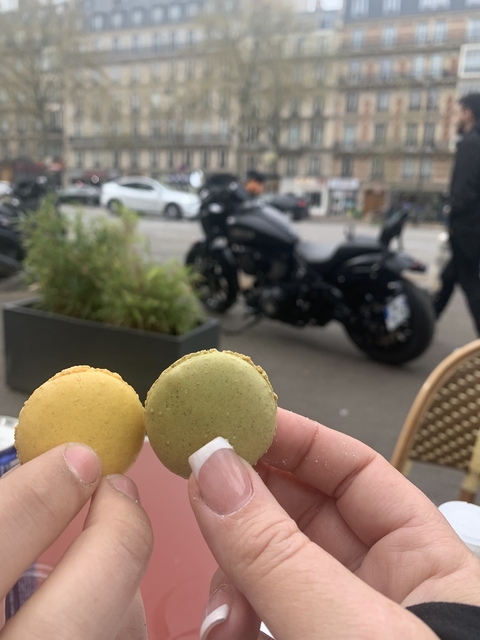 Person holding macarons with a motorcycle blurred in the background