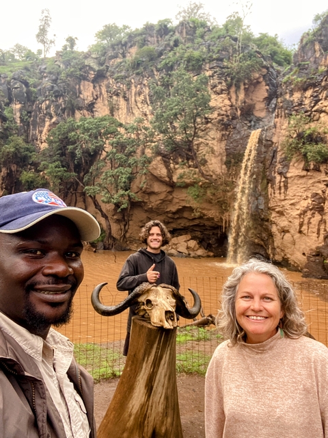 Three people in front of a waterfall with a buffalo skull.