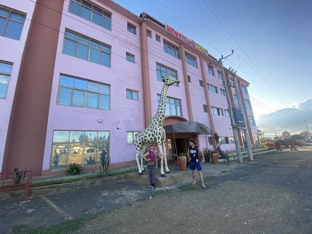 Two people standing beside a giraffe statue in front of a hotel.