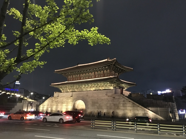 Traditional Asian gate illuminated at night with cars passing by.