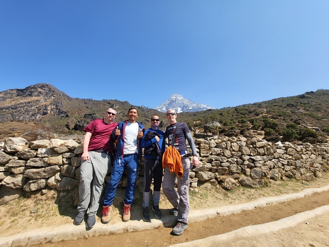 Four people smiling with a mountainous backdrop on a clear day.