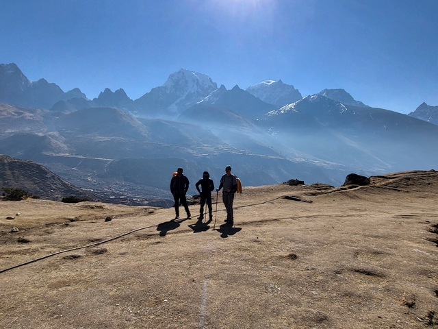 Three people in the foreground with mountain peaks in the background.