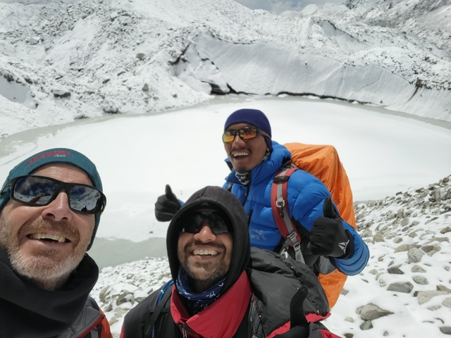 Three people giving thumbs up in a snowy landscape.