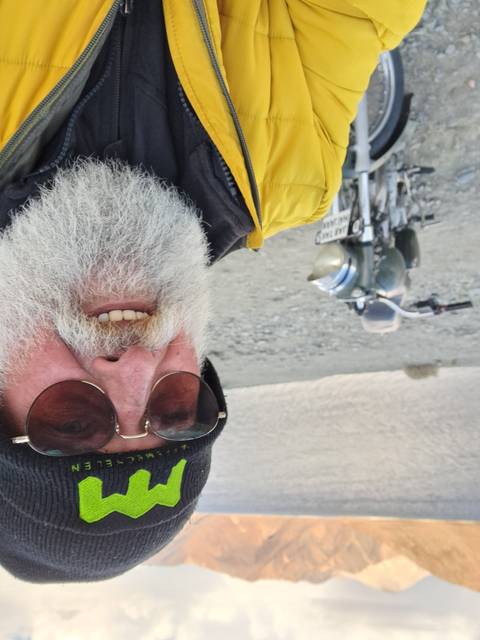 Man posing with a motorcycle in a rocky area.