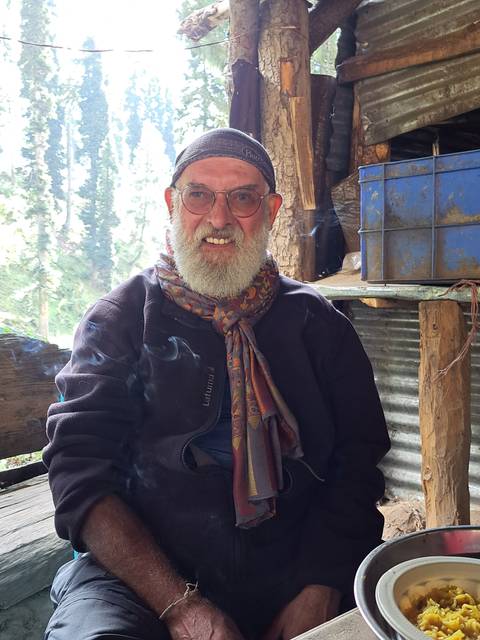 Man smiling while sitting inside a rustic shelter.