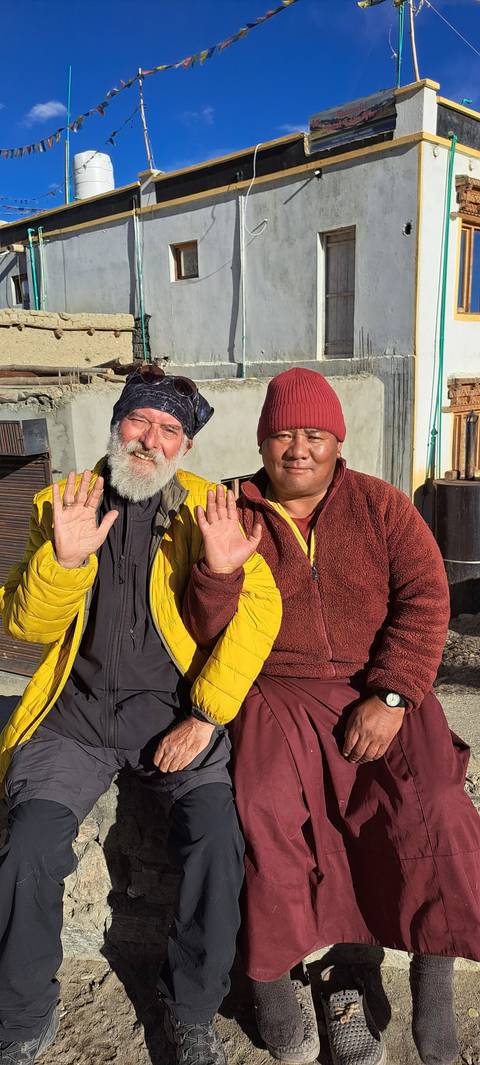 Two people sitting in front of a building, waving.