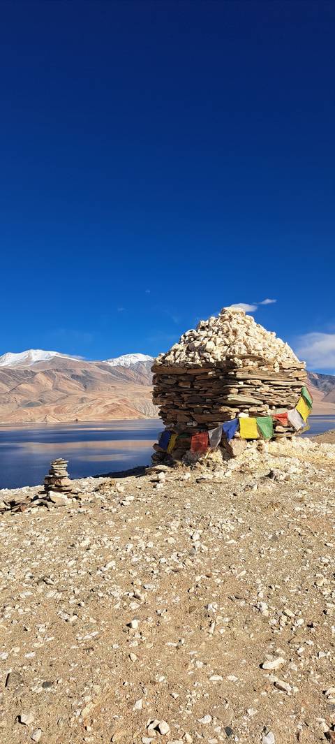 Stone cairn adorned with prayer flags, mountains in the background.