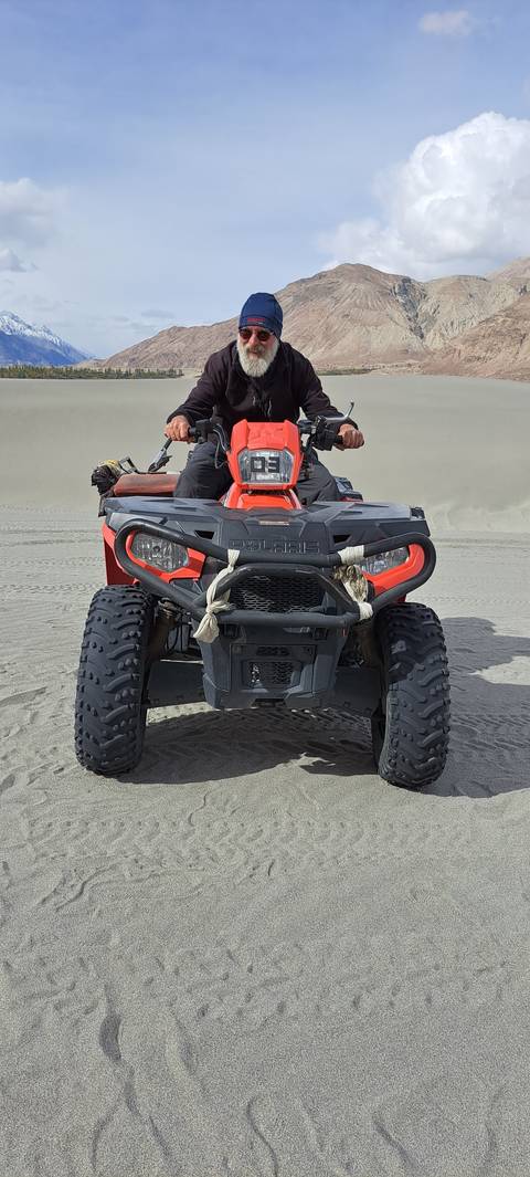 Person riding an ATV across sand dunes.