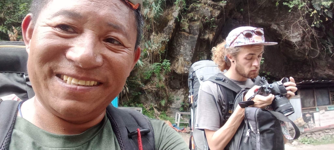 Close-up selfie of two men with outdoor gear on a background of rocks.