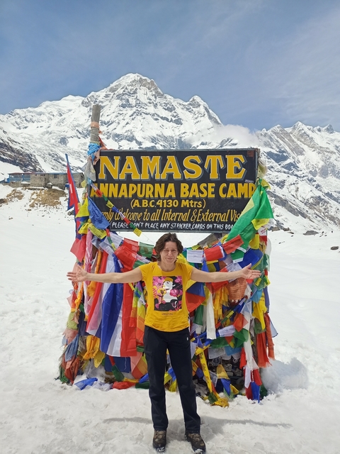 Person standing in front of a sign at Annapurna Base Camp surrounded by snowy mountains.