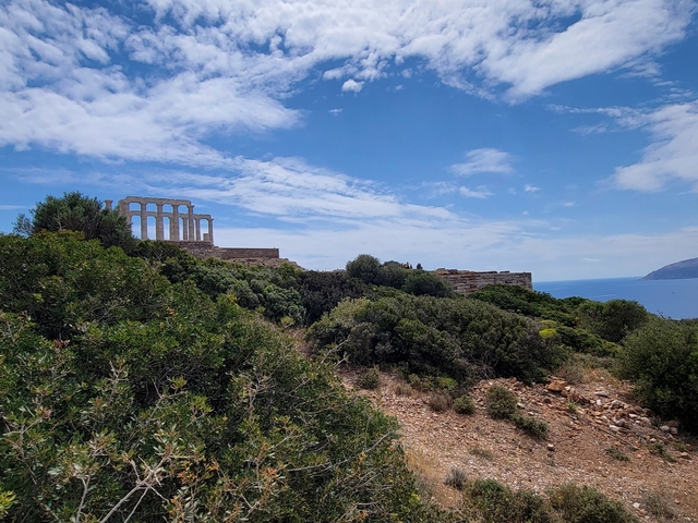 Ancient ruins on a hill overlooking the sea with greenery.