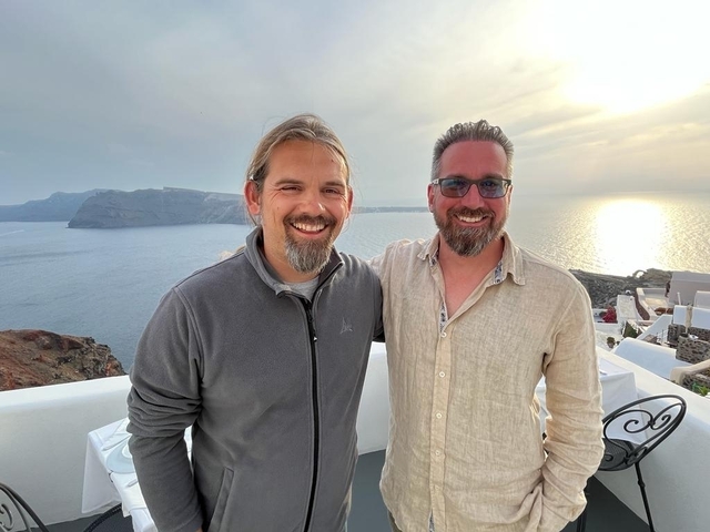 Two men posing with a scenic sea view.