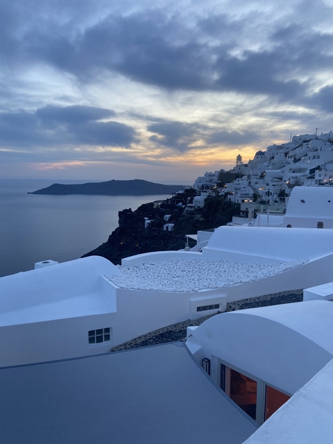 Scenic sunset view of white buildings on a cliff by the sea.