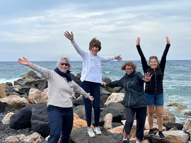 Four women posing by the sea with arms raised.